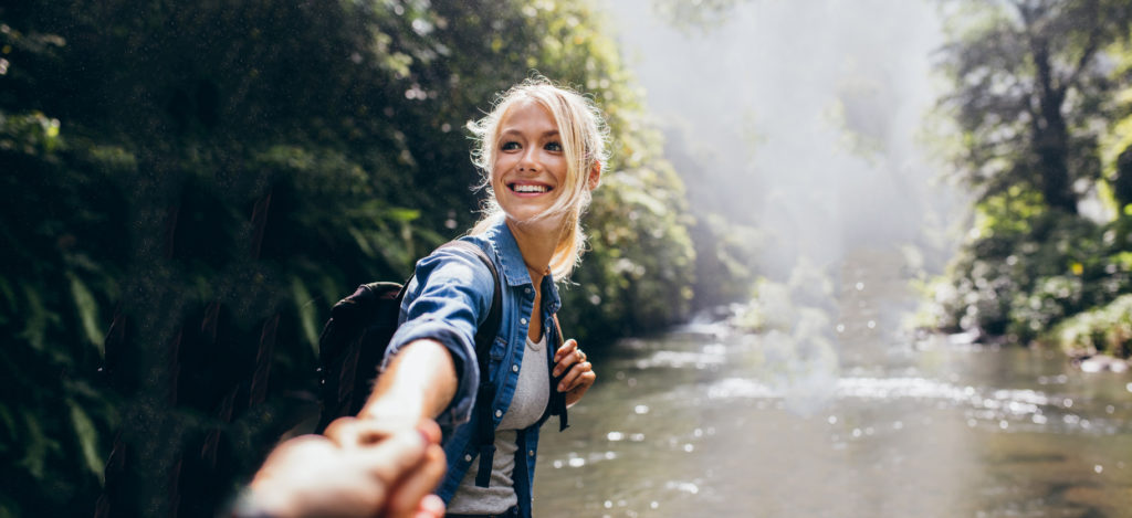 young adult caucasian blonde female leading unknown gender hand towards a creek in a forest