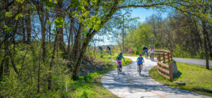 mixed gender, unknown age people riding bikes along a bike trail near a road and a forest